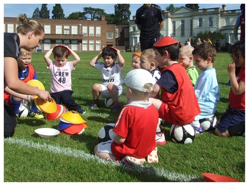 children sat on the grass with a bugs group coach