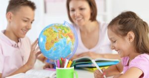 children studying a globe while a teachers watches them