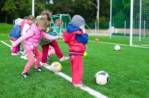 young children kicking footballs towards a goal outdoors