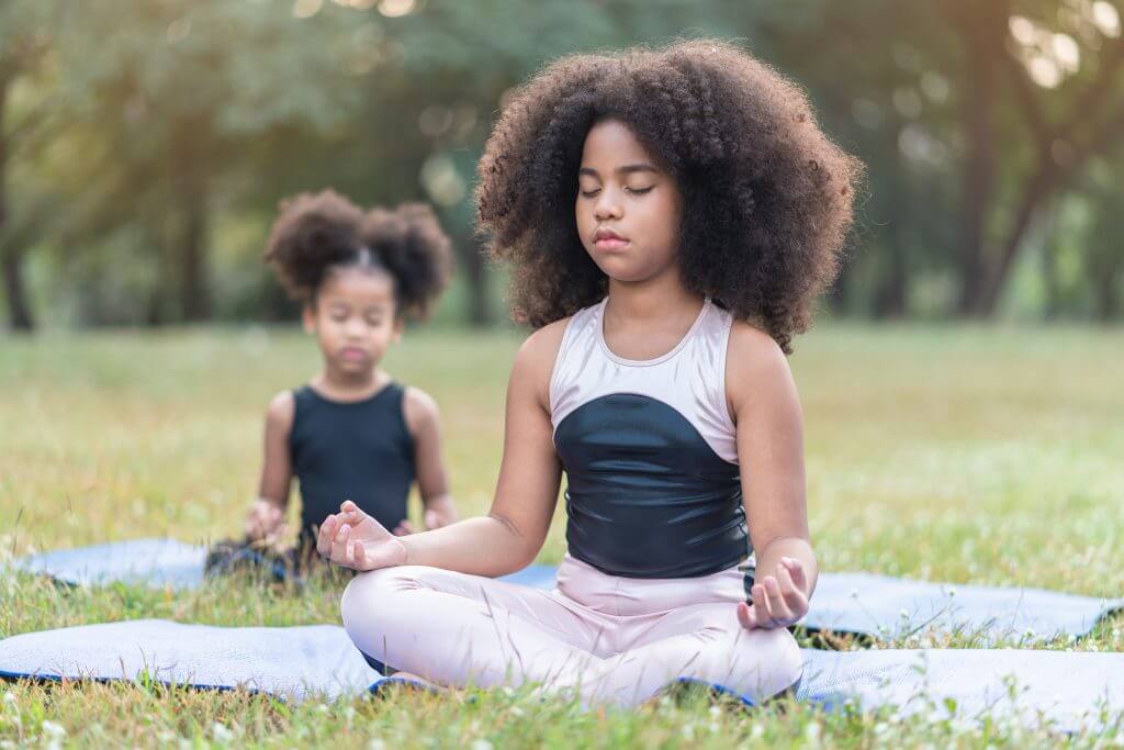 two young girls meditating in a field with their eyes closed