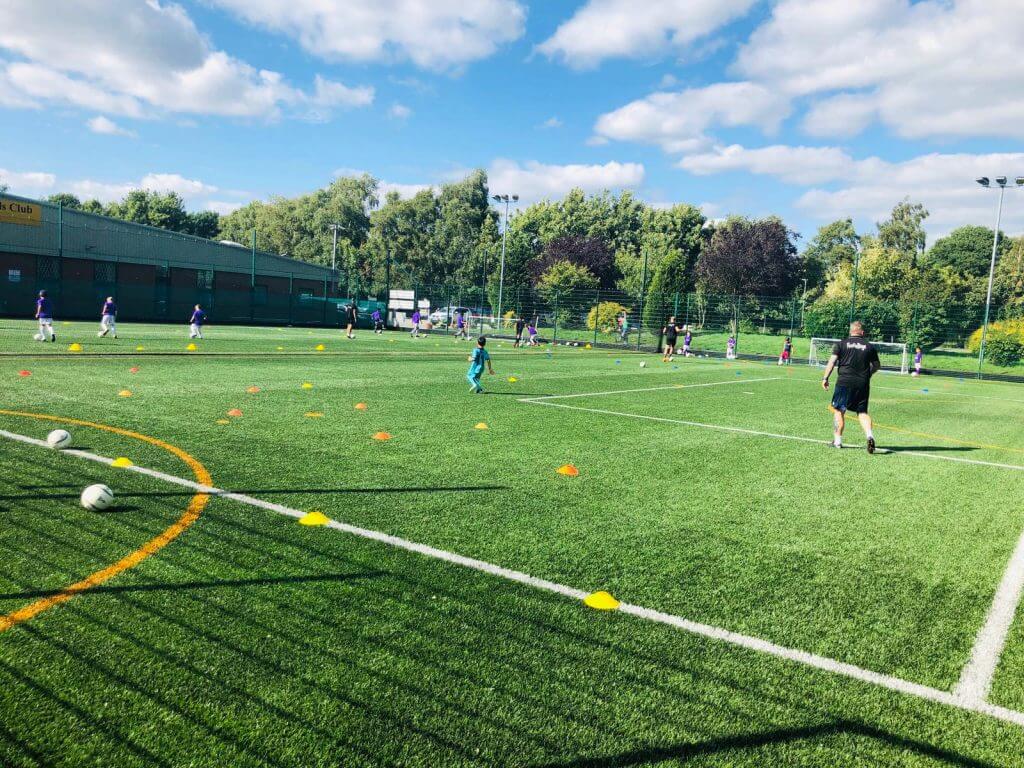 a football pitch at a sports centre with children playing on it and a footiegbugs coach leading the session