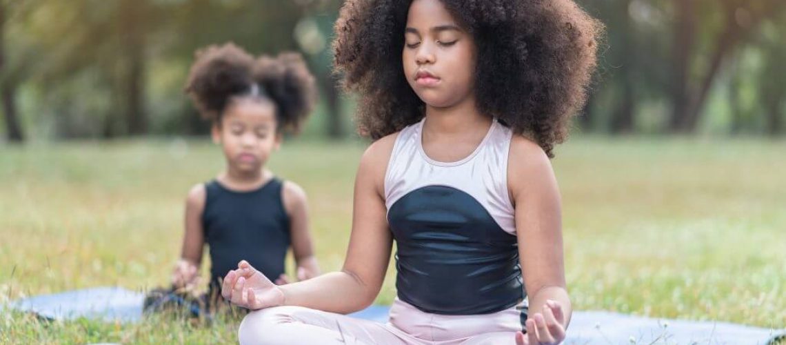 two young girls meditating in a field with their eyes closed
