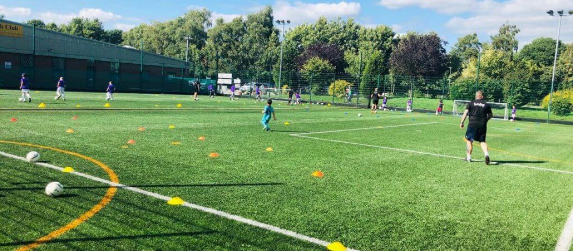 a football pitch at a sports centre with children playing on it and a footiegbugs coach leading the session