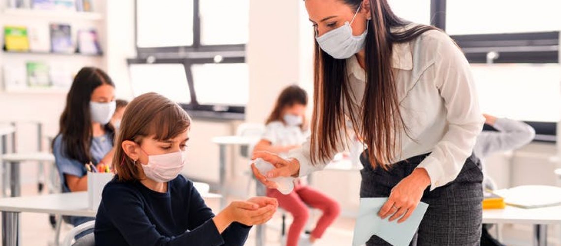 a teacher in a class helping a child sanitize their hands