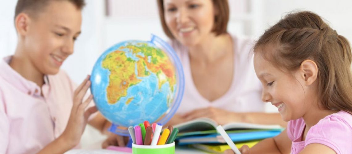 children studying a globe while a teachers watches them