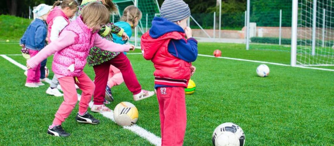 young children kicking footballs towards a goal outdoors